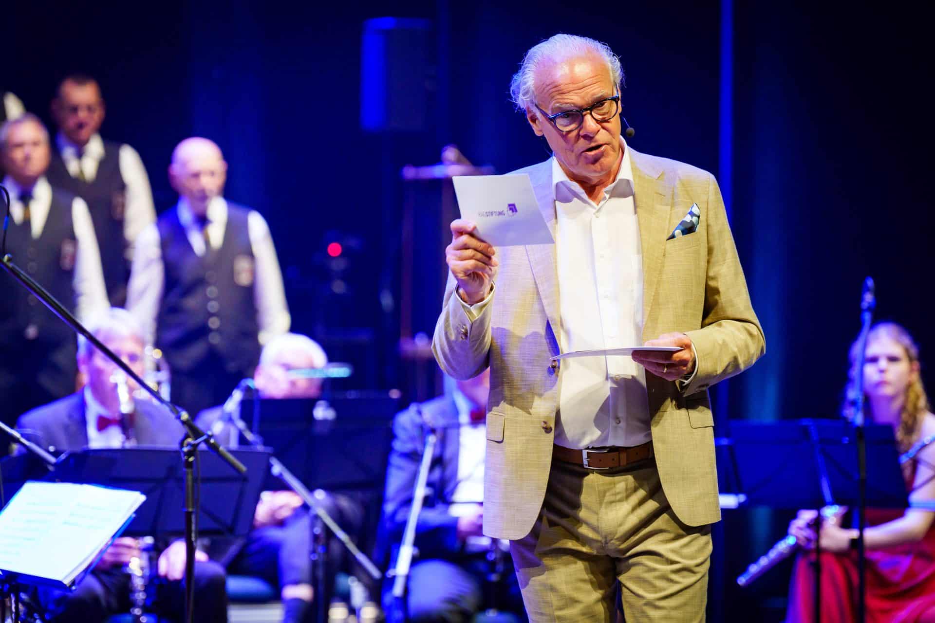 Rolf Schmitz-Malburg moderiert auf der Bühne vor einem Orchester